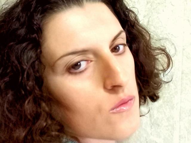 AudreyDaisy has curly brown hair, light skin, brown eyes, and glossy pink lips. She's looking slightly to the side with a subtle, almost bored expression.