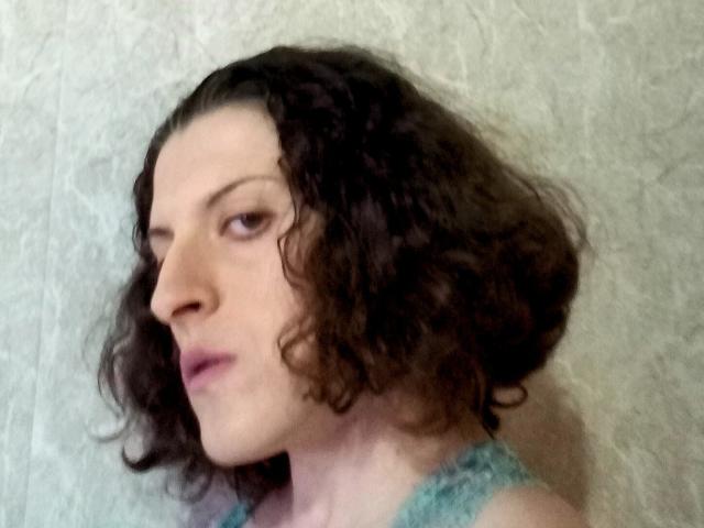 AudreyDaisy has curly brown hair, pale skin, and a pensive expression. She's wearing a teal lace top, looking to the side with subtle pink lipstick.