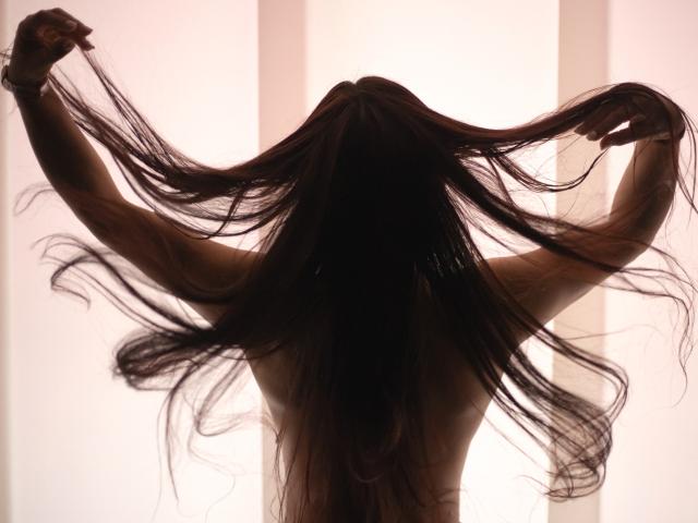 BrianaPreston im Schattenriss, mit langem, dunklem Haar, die Arme heben die Haare, nackt, mit dem Rücken zur Kamera, helles Licht im Hintergrund, weiche Schatten, schlank, sinnlich, fließendes Haar..