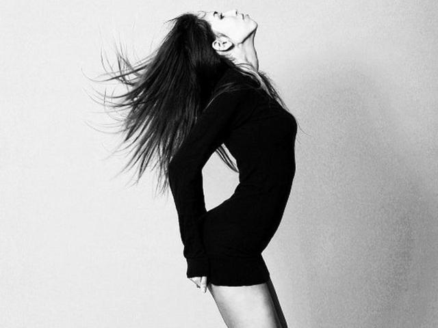 NikaKrasinaS has long, flowing hair, a slender body, and is wearing a tight black dress. She's leaning back, head tilted up, with her ass and tits accentuated.