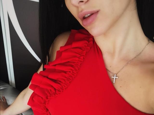 xGabriela com um vestido vermelho com babados, mostrando seus seios e pescoço, usando um colar com uma cruz, cabelo preto, boca ligeiramente aberta, pele clara, sem fundo..