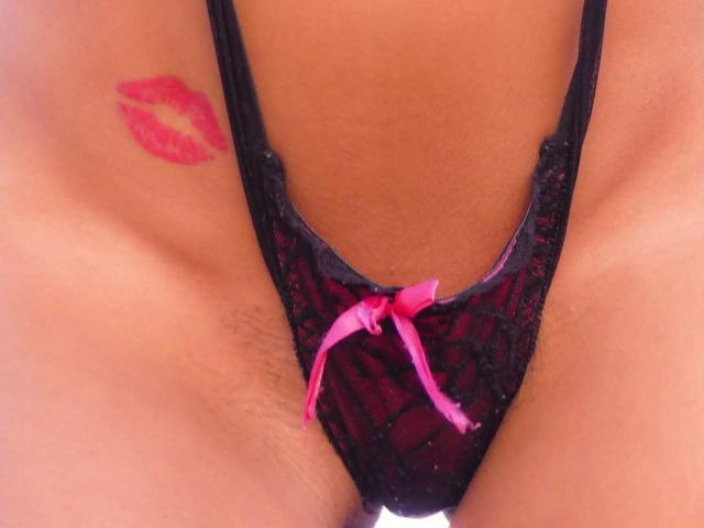CassandraMichelli's black lace thong with pink bow, showing her clean-shaved pussy, and a red lipstick tattoo on her right thigh. Her tan skin is visible.