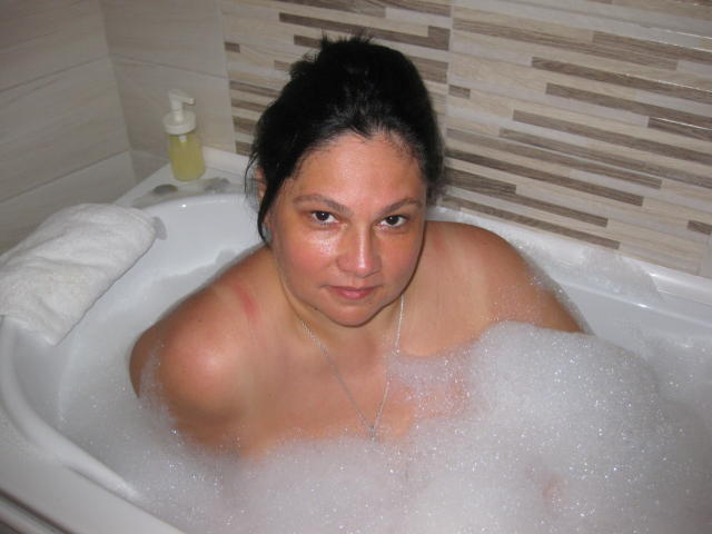 ThiagoYMelissa mit Brüsten in Spitzenunterwäsche und angehobenem Hintern, kniet auf einem Bett. ThiagoYMelissa mit einem kleinen Penis in weißen Boxershorts, steht neben ihr..
