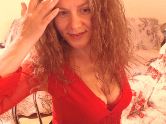 MistressOfShadow's tits in a black lace top, pink lipstick, gold necklace with a key charm, and brown hair. Her boobs are visible, nipples not shown.
