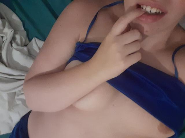 FrancaiseLynne met een blauwe beha die naar beneden is getrokken, waardoor haar borsten zichtbaar zijn, die haar vinger bijt, een klein deel van haar billen laat zien, en een glimp van haar roze geslachtsdeel..