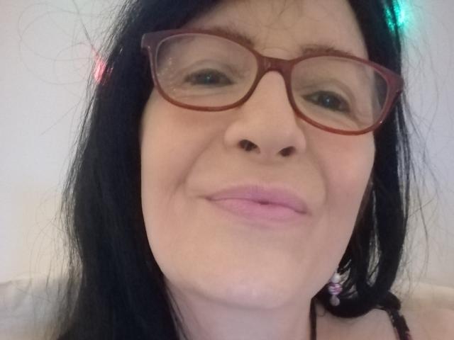 Emilianne, con gafas rojas, cabello negro, labios rosados y una ligera sonrisa, mostrando su nariz y boca. Sus glúteos no son visibles. Tiene un tono de piel claro..