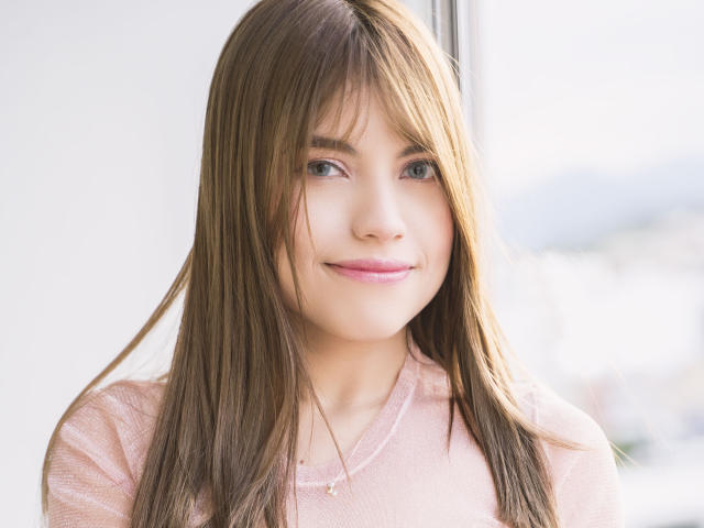 VanityValos con top rosa, ropa interior blanca y calcetines rosas, acostada en una cama blanca, cabello castaño, ojos azules, mirando hacia arriba, mano en la cabeza, globo rosa, almohada blanca..