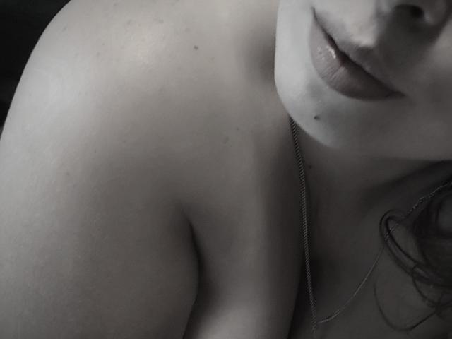 JuliaFrancaise's bare shoulder and upper chest, with a small mole under her lip, and a silver necklace, showing her slightly parted lips in a grayscale photo.