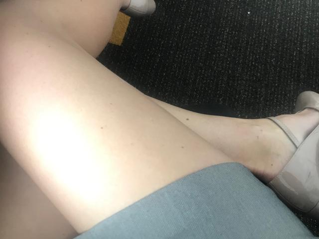 KatieFrenchie's pale legs with small moles, wearing beige flats, and grey shorts, sitting on dark carpeted floor. Her white socks are visible at the top.