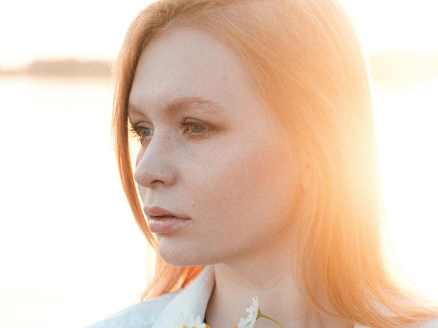 SweetAleksaX heeft bleke huid, rode sproeten en lang oranje haar. Haar ogen zijn blauw en ze draagt een witte blouse met een kleine witte bloem. Ze kijkt naar de zijkant..
