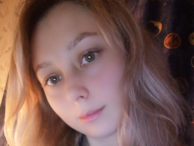 NaozuQAce has light brown hair, green eyes, and a soft pinkish face with slight blush. She's looking at the camera with a subtle, cute smile.