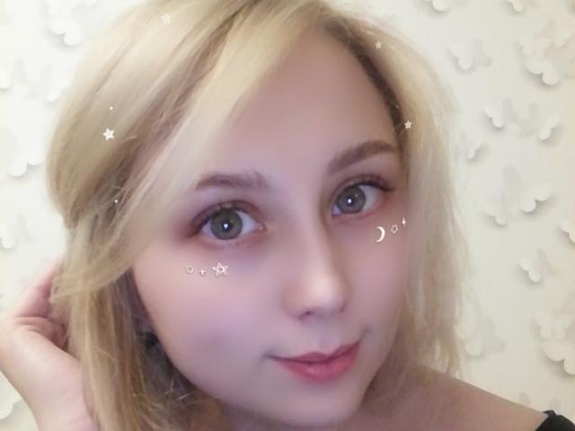 NaozuQAce has blonde hair, blue eyes, and a cute face with a slight smile, wearing a black top, with star and moon digital effects on her cheeks.