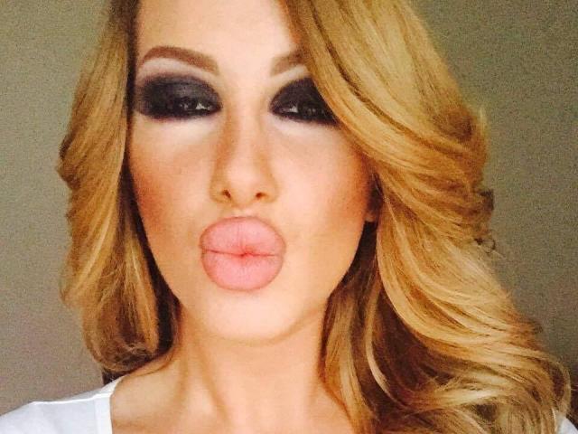 TanyaMonroe with pouty pink lips, blonde wavy hair, and heavy dark smokey eye makeup, looking directly at the camera. Boobs not visible, focus on face.