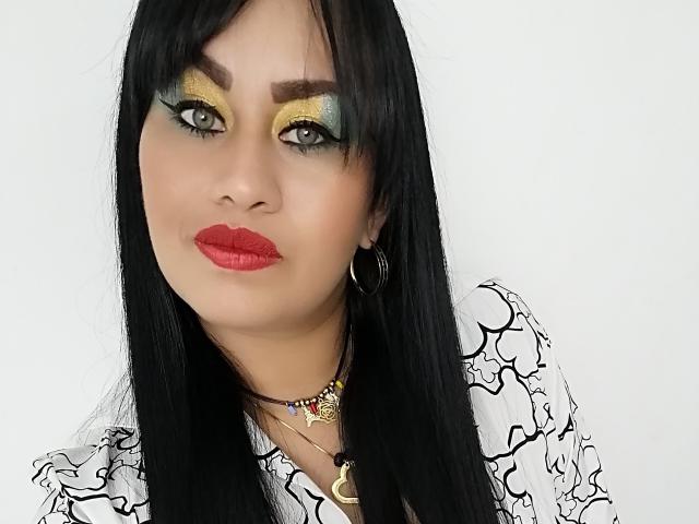 CathyCat has black hair, yellow green eyeshadow, red lipstick, hoop earrings, and a white patterned shirt. She's wearing a necklace with a heart and crescent moon.