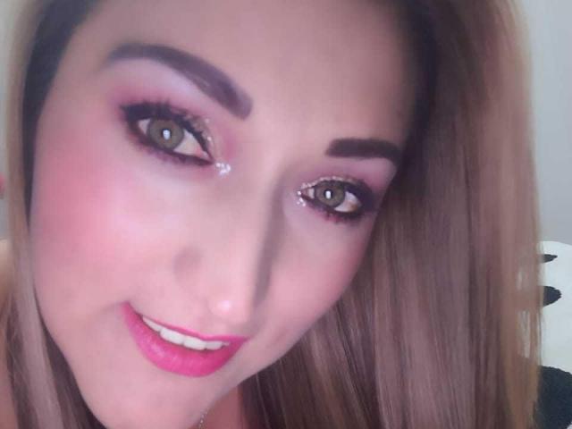 AnnetChau's face with pink eyeshadow, sparkly eyeliner, and pink lipstick, smiling at the camera with brown eyes and blonde hair, slightly angled to the right.
