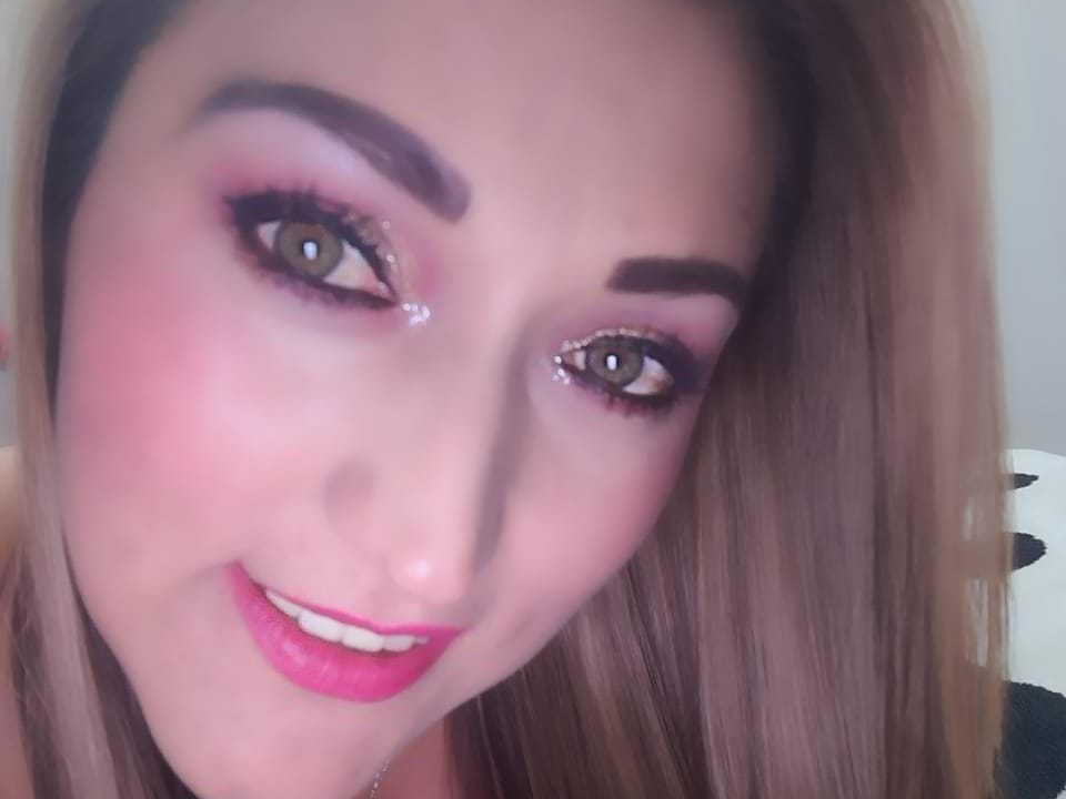 AnnetChau's face with pink eyeshadow, sparkly eyeliner, and pink lipstick, smiling at the camera with brown eyes and blonde hair, slightly angled to the right.