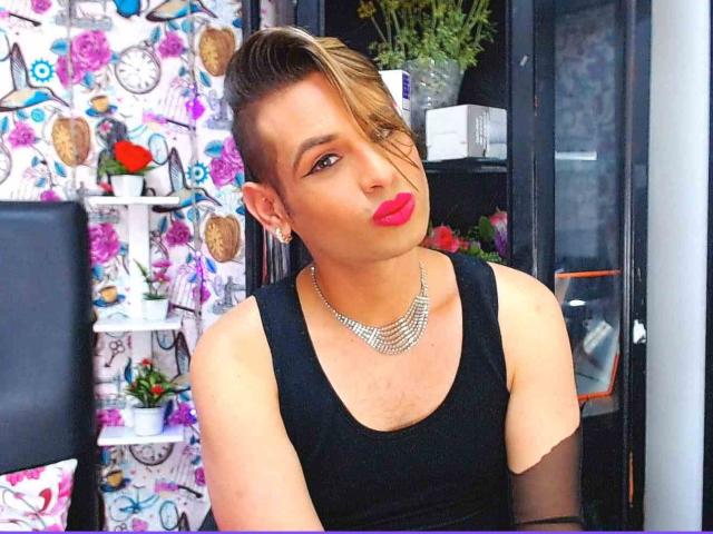 JeanSmithHot with short, blonde-streaked hair, black sleeveless top, shiny necklace, and red lipstick, pouting slightly, showing off smooth, tan skin and a cute, feminine face.