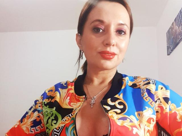 MaitresseBelle a les cheveux bruns, du fard à paupières rose, du rouge à lèvres rouge, et porte une veste colorée et ornée avec un décolleté plongeant, qui révèle ses seins. Elle porte un collier en argent..