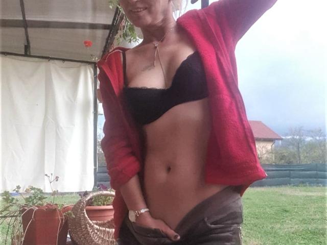 SexyCoco with a red jacket, black bra, and brown pants, pulling down her pants to show her bare, tan-lined, toned midriff and hand in her pants.