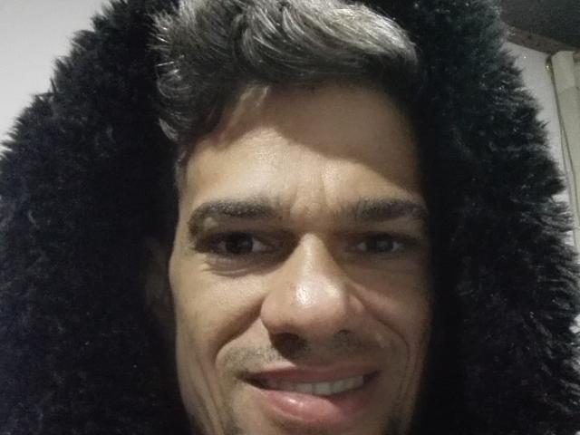 Supercockxx ha i capelli scuri e ricci, un viso leggermente segnato dalle rughe e sta sorridendo mostrando i denti. Il suo naso è lucido e le sue sopracciglia sono folte. Indossa un cappuccio nero di pelliccia..