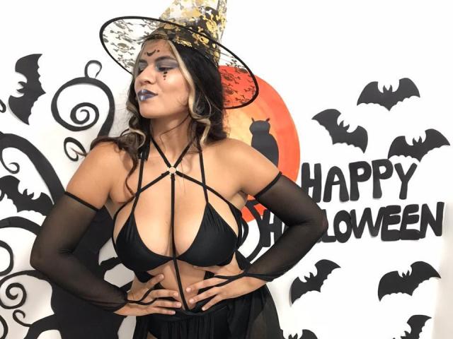 KorinYAmbar with big tits, black strappy bikini, black arm sleeves, gold and black witch hat, dark lipstick, hands on hips, Halloween theme, white background, bats, orange moon.