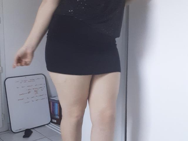 FrancaiseLynne porte un haut noir pailleté et une mini-jupe moulante, laissant apparaître ses cuisses et ses jambes. Son bras droit est légèrement levé. Un tableau blanc se trouve sur la gauche..