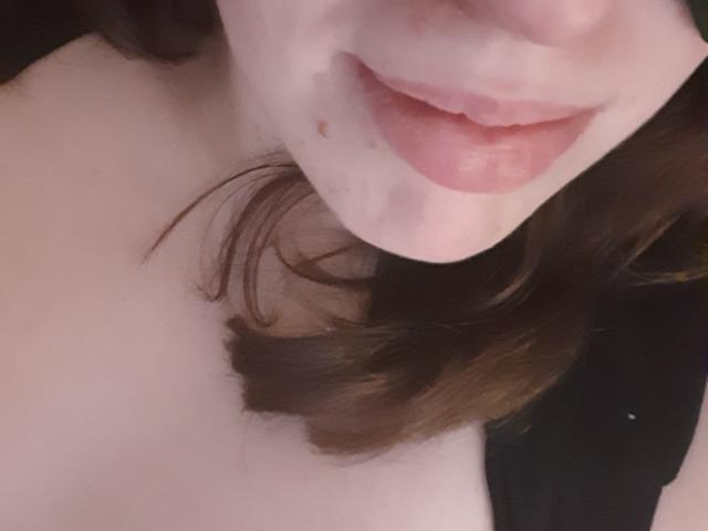 El rostro de Francaise, mostrando sus labios rosados, ligeramente entreabiertos, con una pequeña peca debajo, y su cabello castaño ondulado. Su piel pálida y sus hombros desnudos son visibles..
