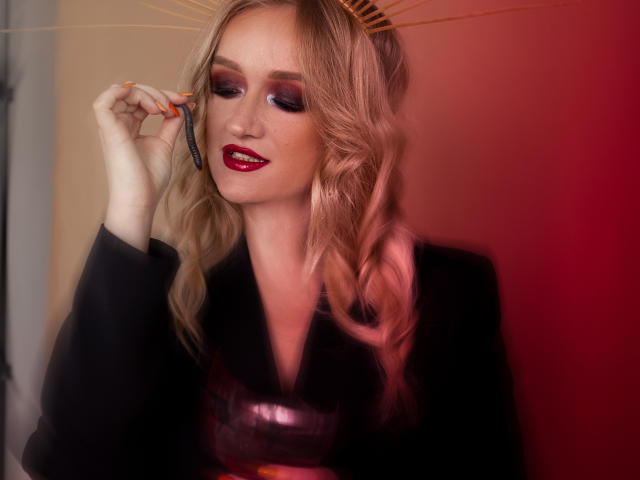 OhMollyHoney with pink hair, red lipstick, and black top, holding a hairbrush, looking down, blushing, and smiling. Her tits are small, and she's sexy as hell.