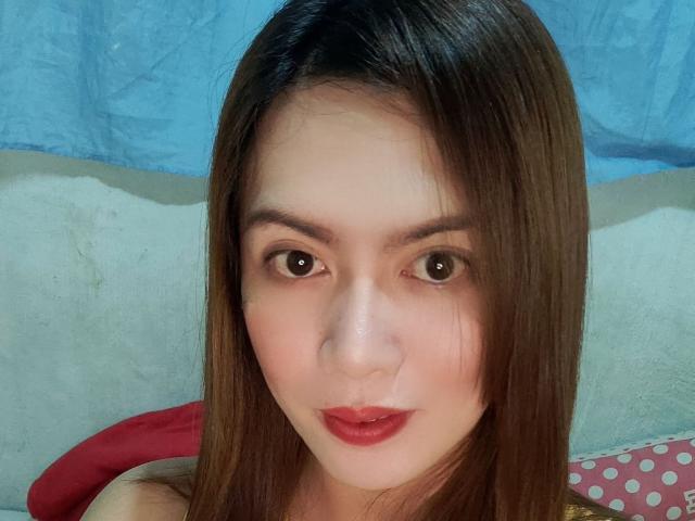 TsHOTLETITIA has brown eyes, straight brown hair, and red lipstick. Her face is centered with a blue background and a red pillow partially visible.