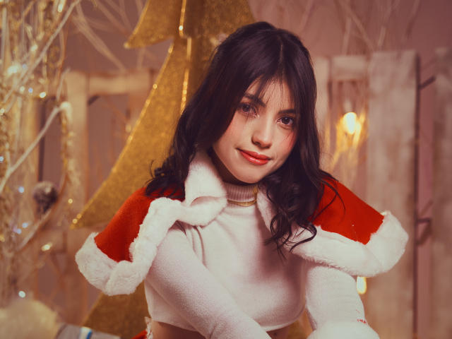 VanityValos met donker, golvend haar, een rode en witte bontrandversierde cape, lachend, met rode lippenstift, een witte coltrui en een schattelijk, aantrekkelijk gezicht. Borsten zichtbaar onder de cape. Kerstthema..