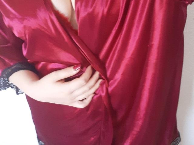 Il vestito di seta rossa di FrancaiseLynne è parzialmente aperto, rivelando il décolleté, e la sua mano stringe delicatamente il tessuto. Le sue unghie sono dipinte di rosso..
