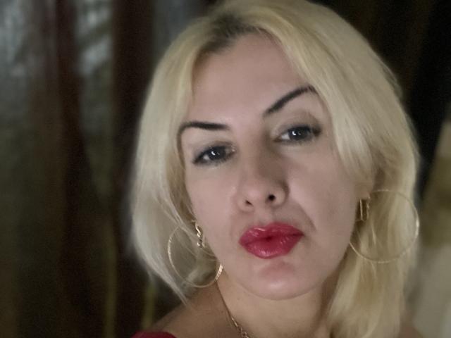 Blond TianaQLove con labbra rosa carnose, sopracciglia nere folte e orecchini a cerchio dorati, che le conferiscono un'aria sensuale. I suoi occhi sono socchiusi e indossa un sottile eyeliner nero..