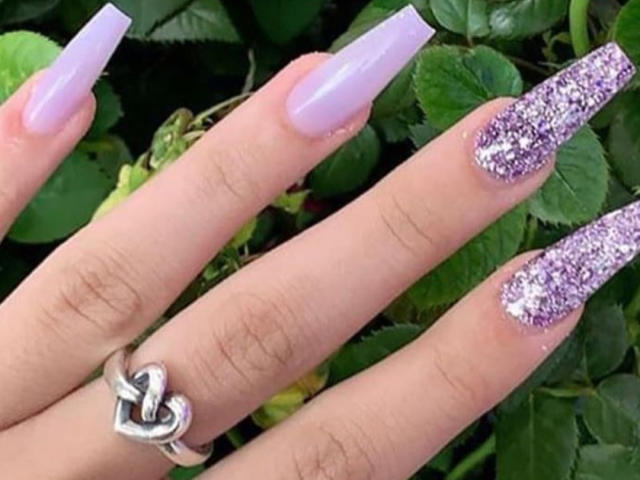 AnastaciaMonaco's hand with long, pale purple nails and glittery purple nails, wearing a heart-shaped ring on her middle finger.