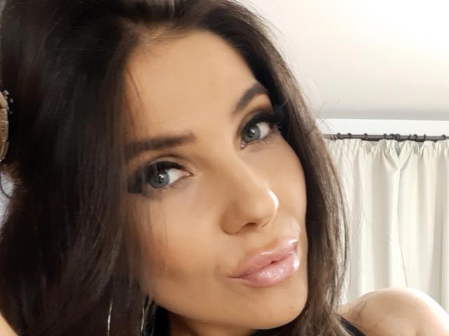 LovelyKinsley has shiny brown eyes, full pink glossy lips, and dark brown hair with a slight updo. Her face is centered, showing a cute, slightly pouty expression.