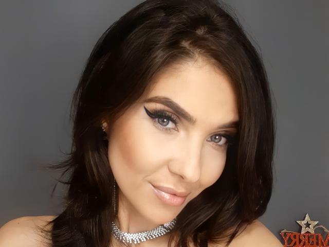 LovelyKinsley heeft donkerbruin haar, blauwe ogen en een lichte glimlach. Ze draagt een glinsterende ketting en heeft dikke, zwarte eyeliner. Haar borsten zijn niet zichtbaar..