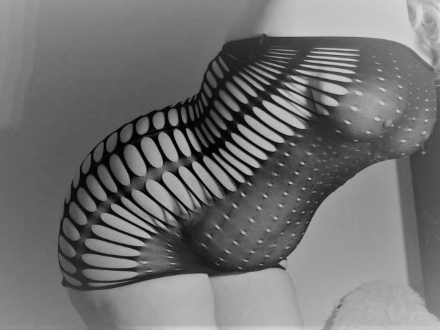 Robe en maille noire avec de grands motifs ovales et à pois, révélant les petites seins et les fesses galbées de JuliaFrancaise. Elle est penchée en avant, montrant son côté et une partie de son dos. Monochrome..