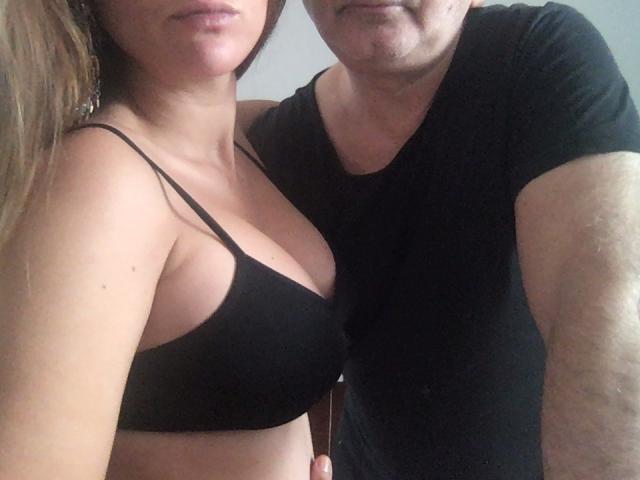 Aria d'amore con una donna formosa in un reggiseno nero e un uomo con una maglietta nera, che stanno vicini, entrambi sorridenti, con il suo braccio intorno a lei, in un selfie..
