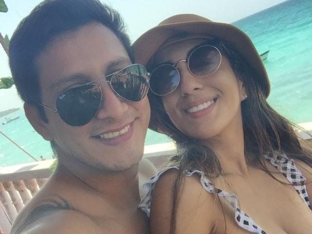 TeequilaCouple69: Hombre sin camisa, con tatuajes y gafas de sol, sonriendo y con piel bronceada, y TeequilaCouple69: mujer de pelo castaño con una camisa a cuadros, sombrero y gafas de sol, ambos en la playa..