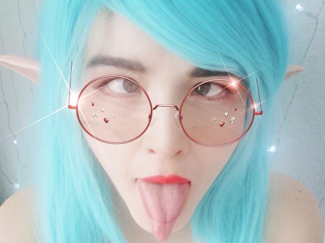 HikaruChan con cabello verde azulado, orejas de elfo rosadas, gafas rojas y la lengua afuera. Labios rojos, ojos brillantes y reflejos de corazones en las gafas. Piel clara, linda y juguetona..