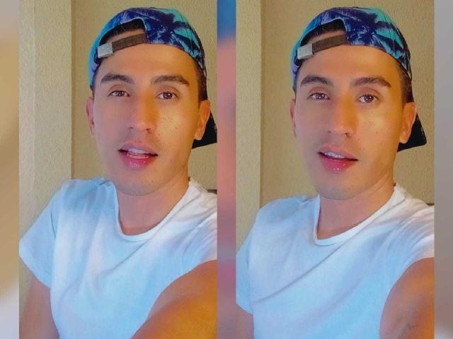 JordanSexyX mit einer blau-schwarzen, gemusterten Kappe, die man von hinten trägt, einem weißen T-Shirt und einem leichten Lächeln, blickt in die Kamera und zeigt ein glattrasiertes Gesicht und braune Augen. Ein Selfie, aufgenommen aus der Seitenperspektive..