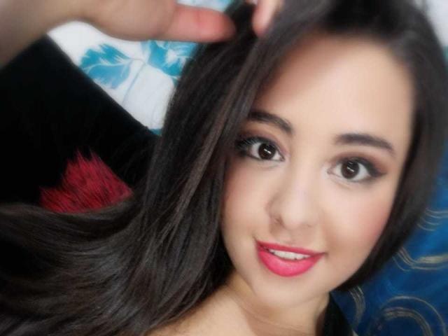 Santa Rodrigues tiene el pelo largo y castaño, ojos oscuros, lápiz labial rosa y un piercing en la nariz, con una mano tocando suavemente su cabello. Está sonriendo y mirando a la cámara..
