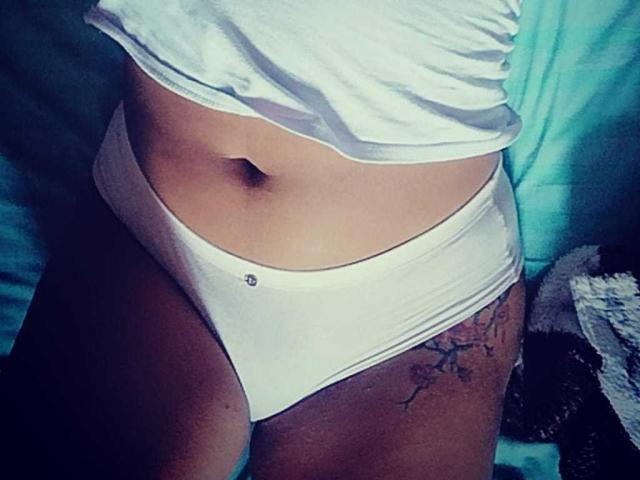 Shalyn's white panties, showing her flat stomach and a small tattoo on her right thigh, with a white shirt slightly lifted. Her navel is visible.