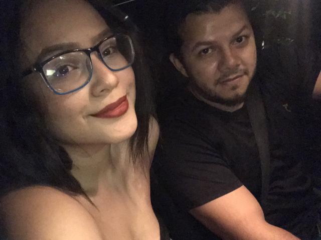 ValenDirty con gli occhiali, il rossetto rosso e i capelli neri, che sorride alla fotocamera. Accanto a lei, ValenDirty con i capelli corti e scuri, la barba e la maglietta nera, che sorride leggermente..