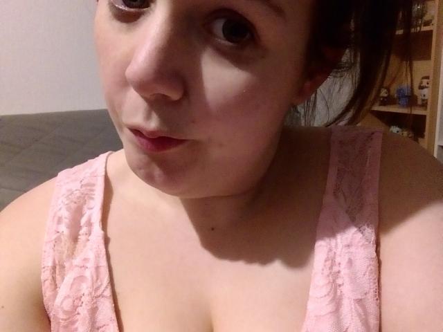 LoveClo, com pele clara e olhos castanhos, vestindo uma blusa de renda rosa, mostrando seus seios e com um leve semblante de descontentamento, com o cabelo preso..