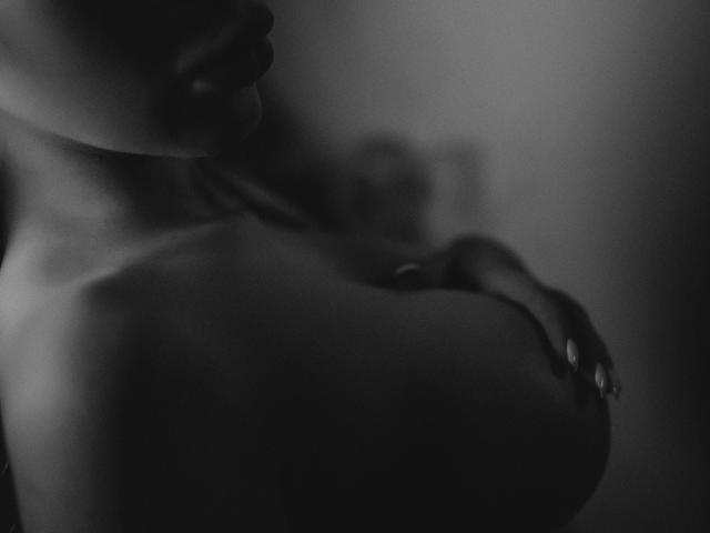 GoddessKaterina's dark-skinned, bare tits are prominently featured in a black-and-white, blurry, close-up shot. Her hand gently rests on her right tit.
