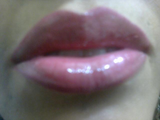 MelissaDelici's glossy, plump, pinkish-red lips with a slight sheen, centered in the image. Her upper teeth are visible, adding a subtle, sexy touch.