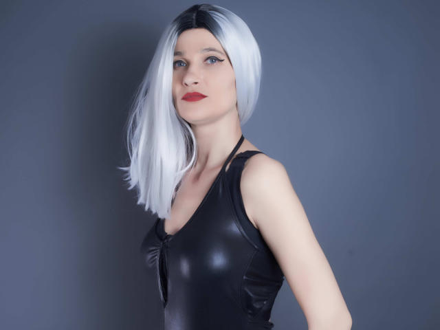 MistressKate with silver bob, black leather top, red lips, pale skin, and blue eyes, looking straight at the camera. Boobs are small, tits are flat, pussy is not visible.