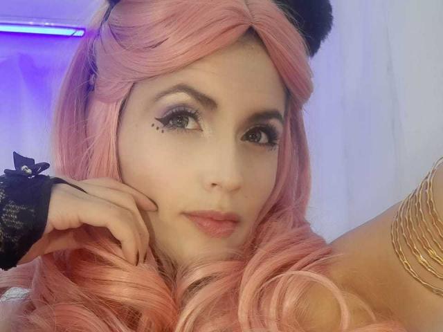 LinaStars with pink hair, black cat ears, and a cute face, wearing a black wristband and a gold arm band, has her chin on her hand, looking at the camera.