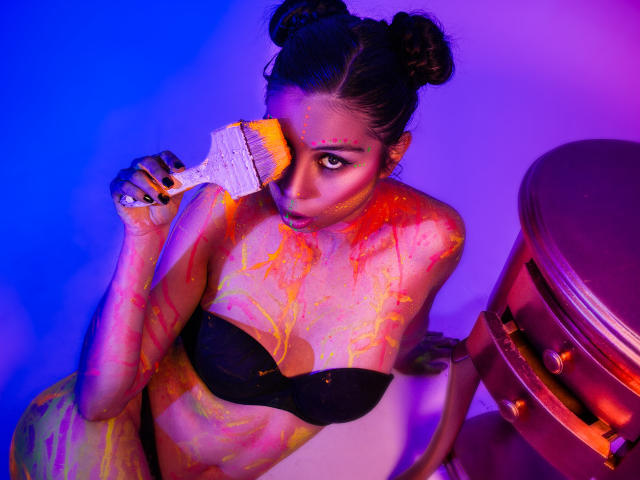 IsaTimeSweet with painted body, black bra, holding paintbrush in eye, purple-blue lighting, double buns, looking at camera, paint splattered on tits and chest, paintbrush in hand.