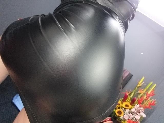 El brillante trasero de cuero negro de LeiizaMistress está prominentemente en primer plano, con su trasero apretado, curvado y reflectante ocupando la mayor parte del encuadre..